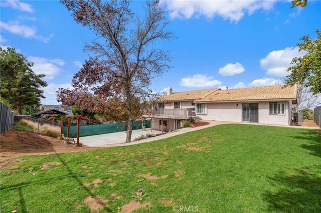 rear view of property with fence, a tiled roof, stucco siding, a lawn, and a patio