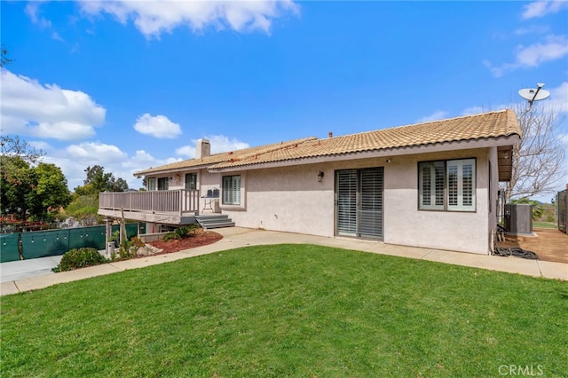 rear view of property featuring stucco siding, a lawn, a deck, a tile roof, and fence