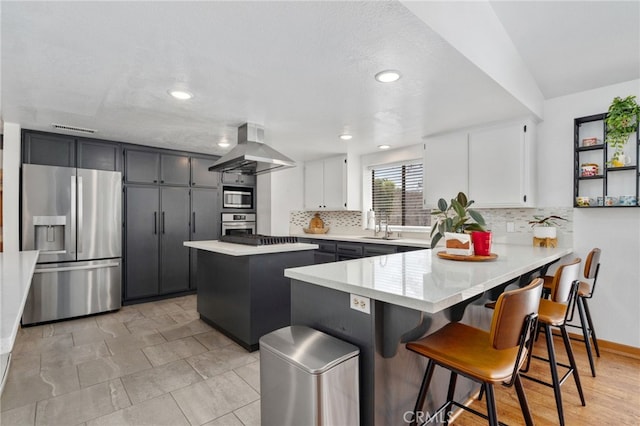 kitchen with visible vents, island exhaust hood, a sink, appliances with stainless steel finishes, and a peninsula