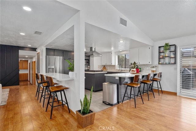 kitchen featuring visible vents, stainless steel fridge with ice dispenser, a breakfast bar, a peninsula, and exhaust hood