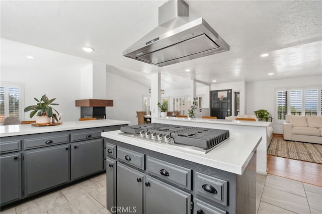 kitchen with gray cabinetry, a kitchen island, wall chimney range hood, stainless steel gas cooktop, and open floor plan