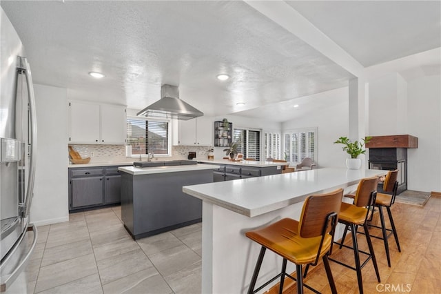 kitchen with gray cabinetry, a kitchen island, stainless steel fridge with ice dispenser, a breakfast bar area, and a peninsula