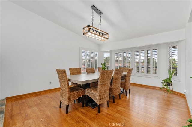 dining room with vaulted ceiling, a healthy amount of sunlight, light wood-style floors, and baseboards