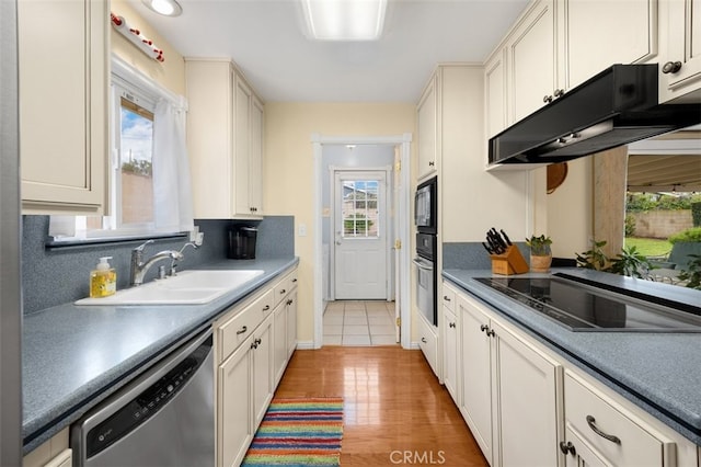 kitchen with a sink, black appliances, light wood-style floors, under cabinet range hood, and tasteful backsplash