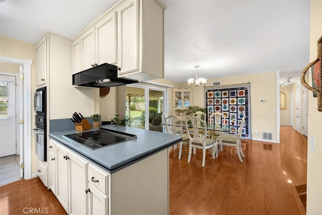 kitchen featuring a healthy amount of sunlight, wood finished floors, black appliances, under cabinet range hood, and a chandelier