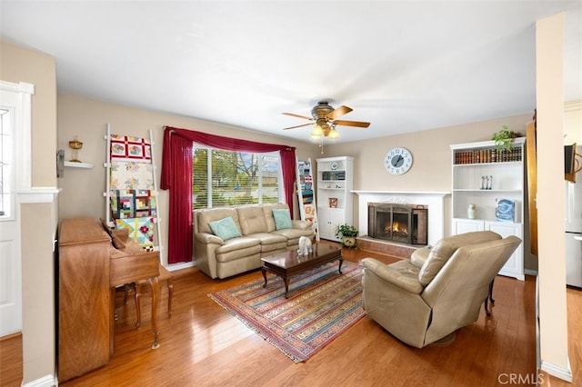 living room with a warm lit fireplace, ceiling fan, and light wood finished floors