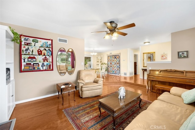 living area with visible vents, ceiling fan with notable chandelier, baseboards, and wood finished floors