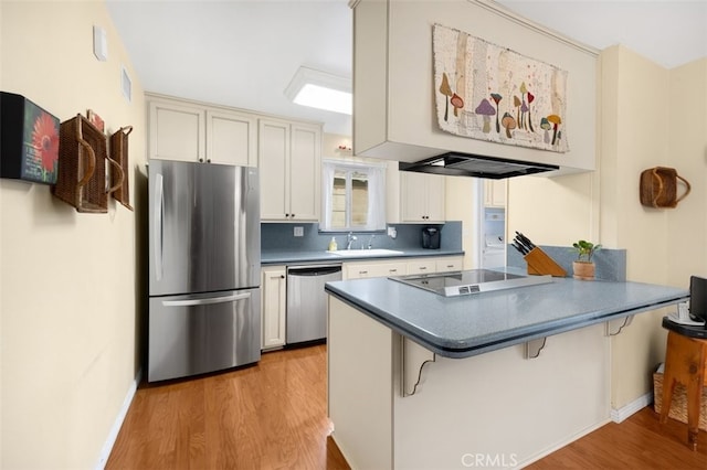 kitchen with light wood finished floors, a peninsula, a sink, stainless steel appliances, and tasteful backsplash