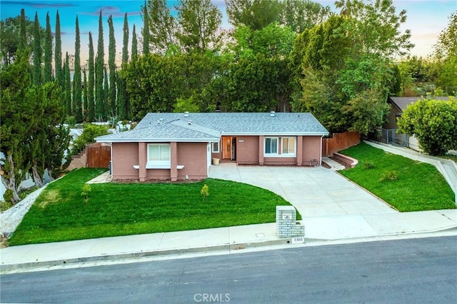 ranch-style house featuring stucco siding, driveway, a front yard, and fence