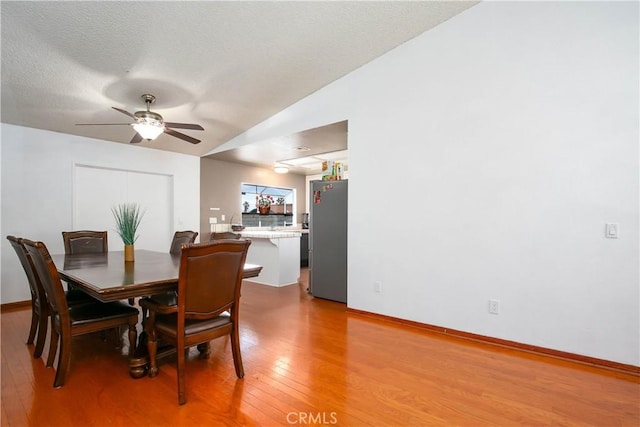 dining room featuring lofted ceiling, a ceiling fan, a textured ceiling, light wood finished floors, and baseboards