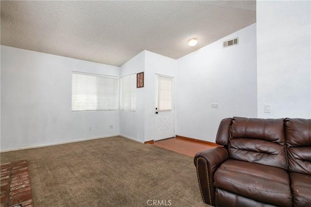 sitting room with vaulted ceiling, carpet flooring, visible vents, and a textured ceiling