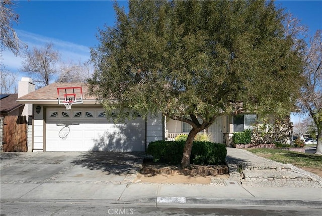 view of property hidden behind natural elements with a chimney, concrete driveway, and a garage