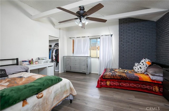 bedroom featuring a ceiling fan, wood finished floors, brick wall, lofted ceiling with beams, and a textured ceiling