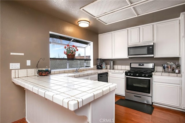 kitchen with wood finished floors, a peninsula, a sink, appliances with stainless steel finishes, and white cabinetry