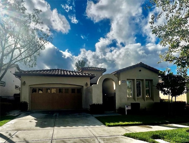 mediterranean / spanish-style home featuring a tile roof, a garage, driveway, and stucco siding