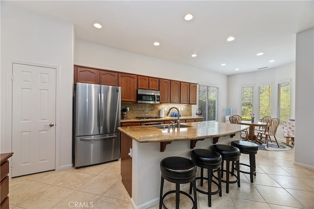 kitchen featuring a breakfast bar area, a sink, decorative backsplash, appliances with stainless steel finishes, and light tile patterned floors
