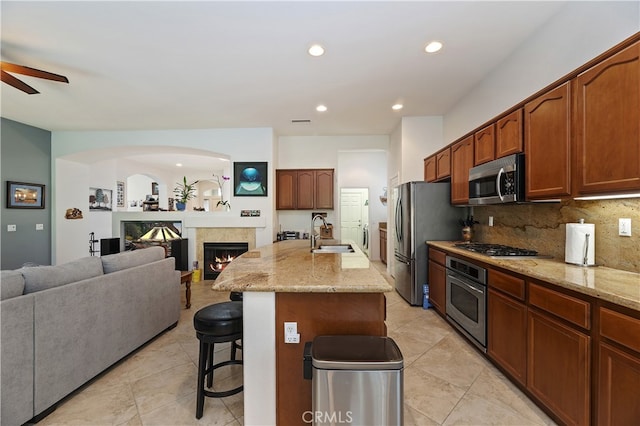 kitchen featuring stainless steel appliances, a breakfast bar, a sink, light stone countertops, and open floor plan
