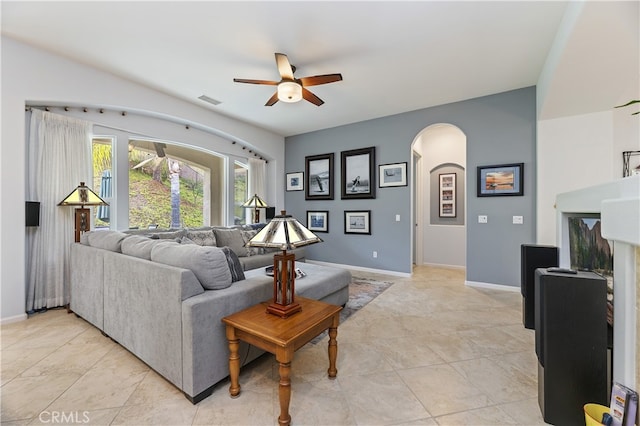 living room featuring arched walkways, baseboards, visible vents, a ceiling fan, and light tile patterned floors