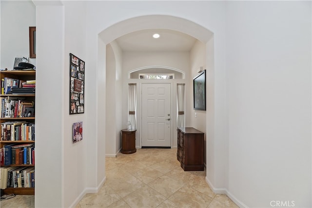 corridor featuring baseboards, arched walkways, and light tile patterned floors