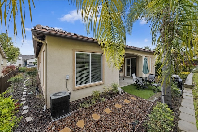 rear view of property featuring central AC unit, fence, a tiled roof, stucco siding, and a patio area