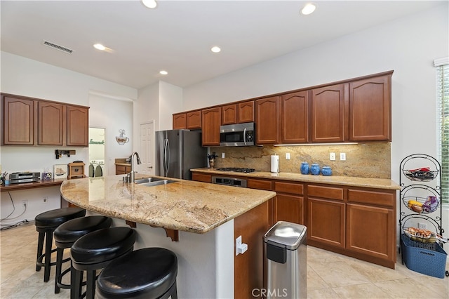 kitchen featuring a sink, light stone countertops, decorative backsplash, appliances with stainless steel finishes, and a breakfast bar area