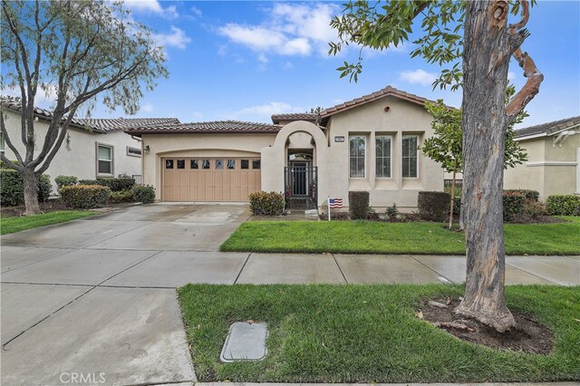 mediterranean / spanish house featuring stucco siding, a front lawn, driveway, an attached garage, and a tiled roof