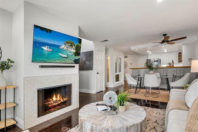 living room with a ceiling fan, wood finished floors, baseboards, and a tile fireplace