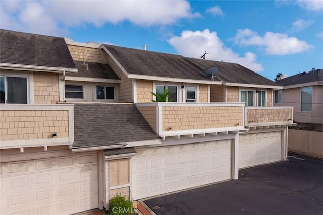 view of property with aphalt driveway, a balcony, a shingled roof, and a garage