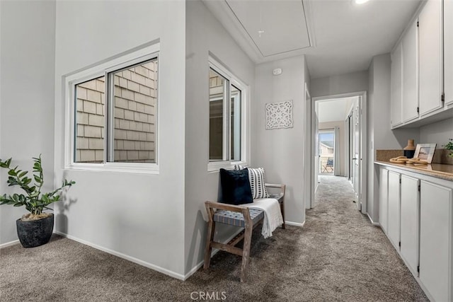 corridor featuring carpet flooring, attic access, and baseboards