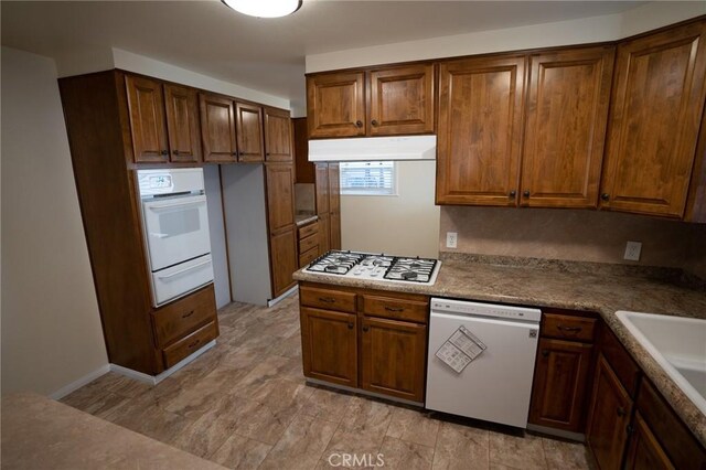 kitchen featuring under cabinet range hood, brown cabinetry, white appliances, a warming drawer, and a sink