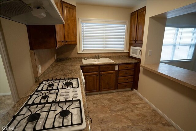 kitchen featuring white microwave, under cabinet range hood, stovetop, brown cabinets, and a sink