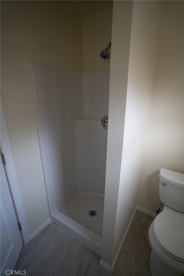 full bathroom with a stall shower, toilet, and baseboards