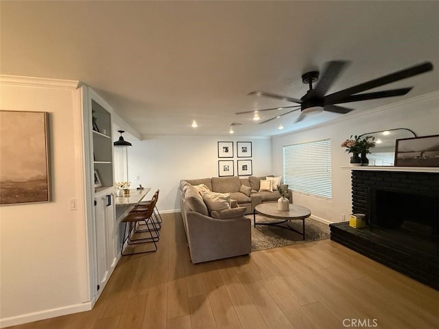 living area featuring a ceiling fan, wood finished floors, baseboards, ornamental molding, and a brick fireplace