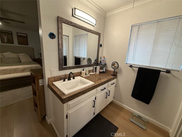 bathroom with ornamental molding, a ceiling fan, wood finished floors, baseboards, and vanity