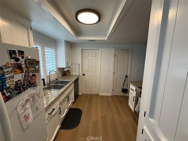 kitchen with black dishwasher, light wood-style flooring, freestanding refrigerator, a raised ceiling, and a sink