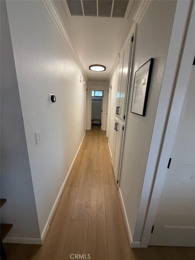 hallway featuring visible vents, crown molding, light wood-type flooring, and baseboards