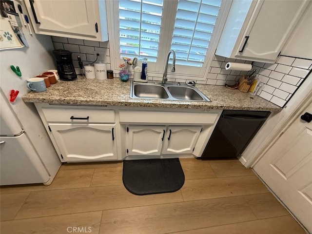 kitchen featuring tasteful backsplash, light wood-style flooring, freestanding refrigerator, white cabinets, and a sink