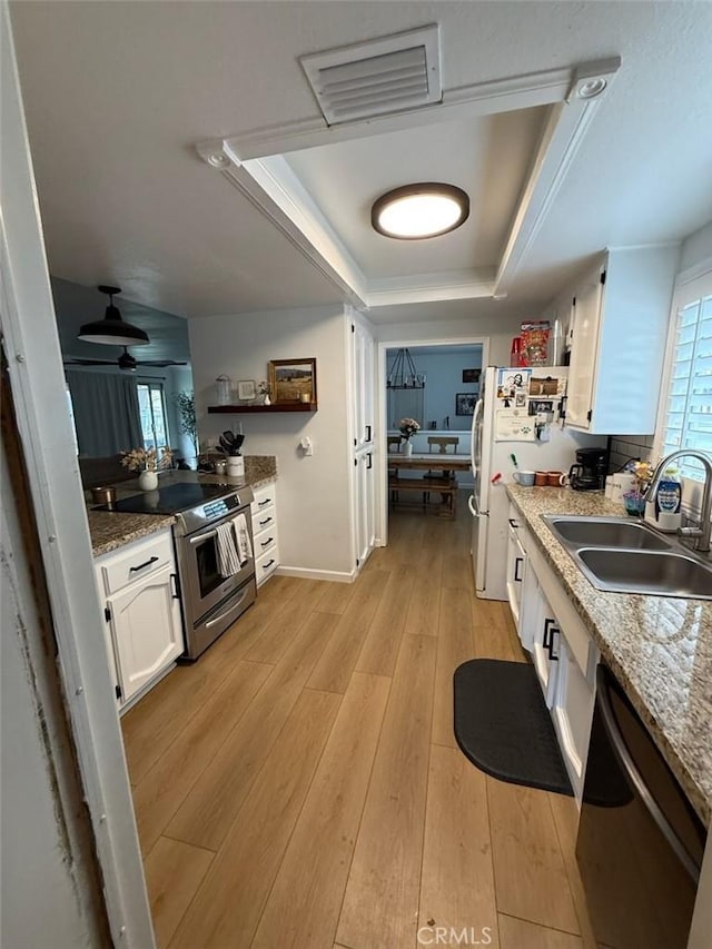 kitchen with a sink, open shelves, a tray ceiling, appliances with stainless steel finishes, and light wood finished floors