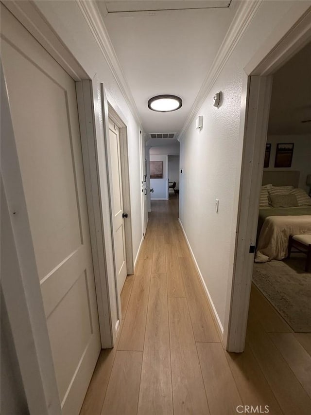 corridor with light wood finished floors, visible vents, crown molding, and baseboards