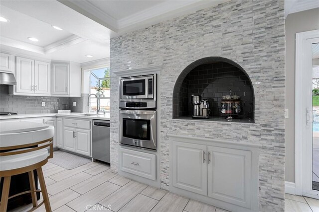 kitchen with white cabinetry, stainless steel appliances, crown molding, and a sink