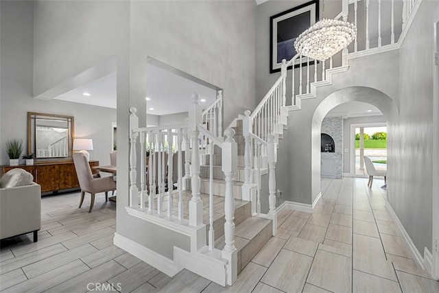 stairs featuring arched walkways, a towering ceiling, baseboards, and wood tiled floor