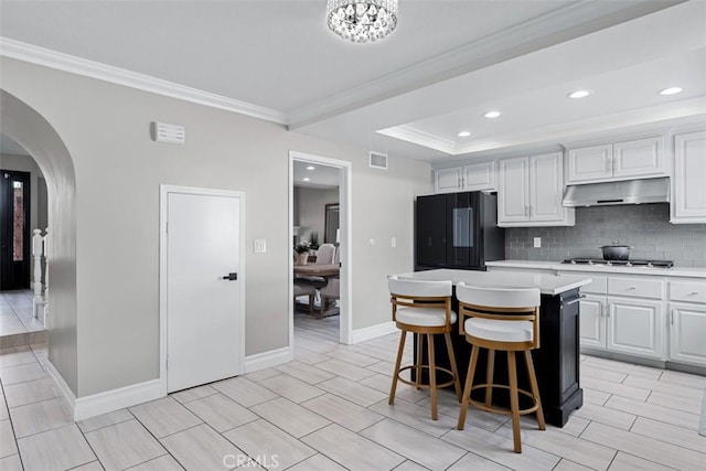 kitchen with under cabinet range hood, black refrigerator, a kitchen island, arched walkways, and stainless steel gas cooktop