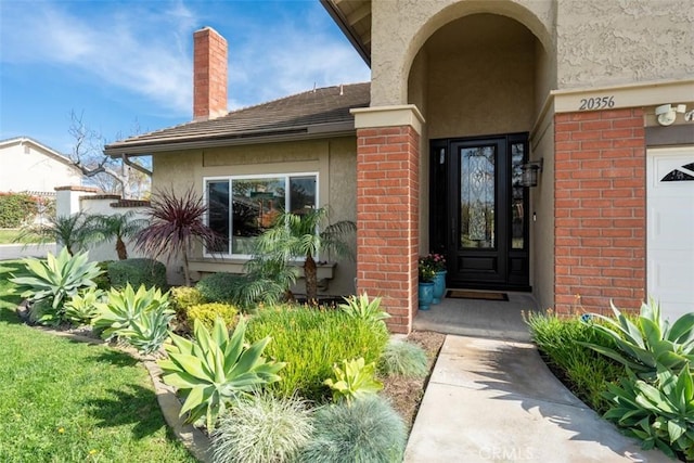 property entrance featuring stucco siding, brick siding, a garage, and a chimney