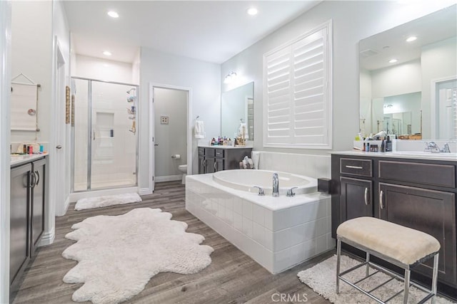 bathroom with a garden tub, wood finished floors, toilet, and a stall shower