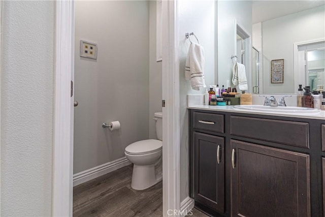 bathroom featuring toilet, vanity, baseboards, and wood finished floors