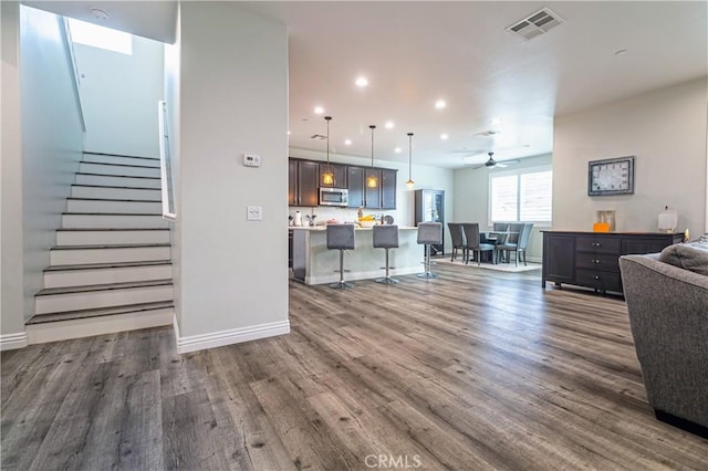 living area with visible vents, dark wood-style flooring, a ceiling fan, and stairway