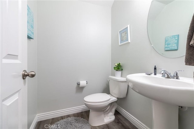 half bathroom featuring a sink, toilet, baseboards, and wood finished floors