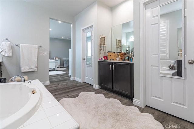 full bath with baseboards, a garden tub, wood finished floors, and vanity