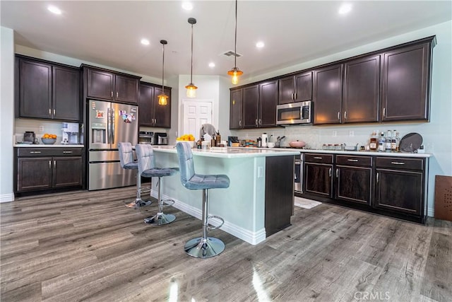 kitchen featuring a kitchen bar, dark brown cabinetry, wood finished floors, and stainless steel appliances