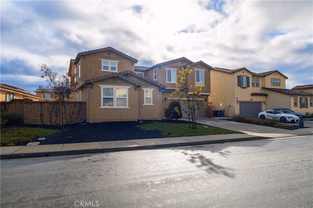 view of front of property with stucco siding, driveway, fence, a residential view, and an attached garage